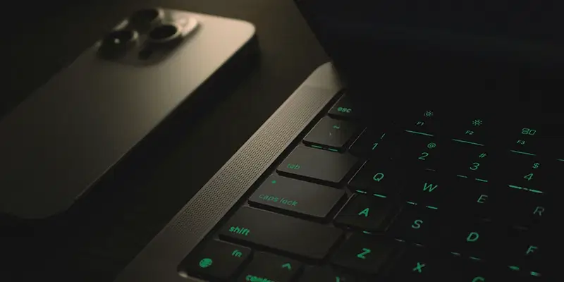 Illuminated laptop keyboard beside a smartphone, both showcasing a sleek, modern design in a dark setting.