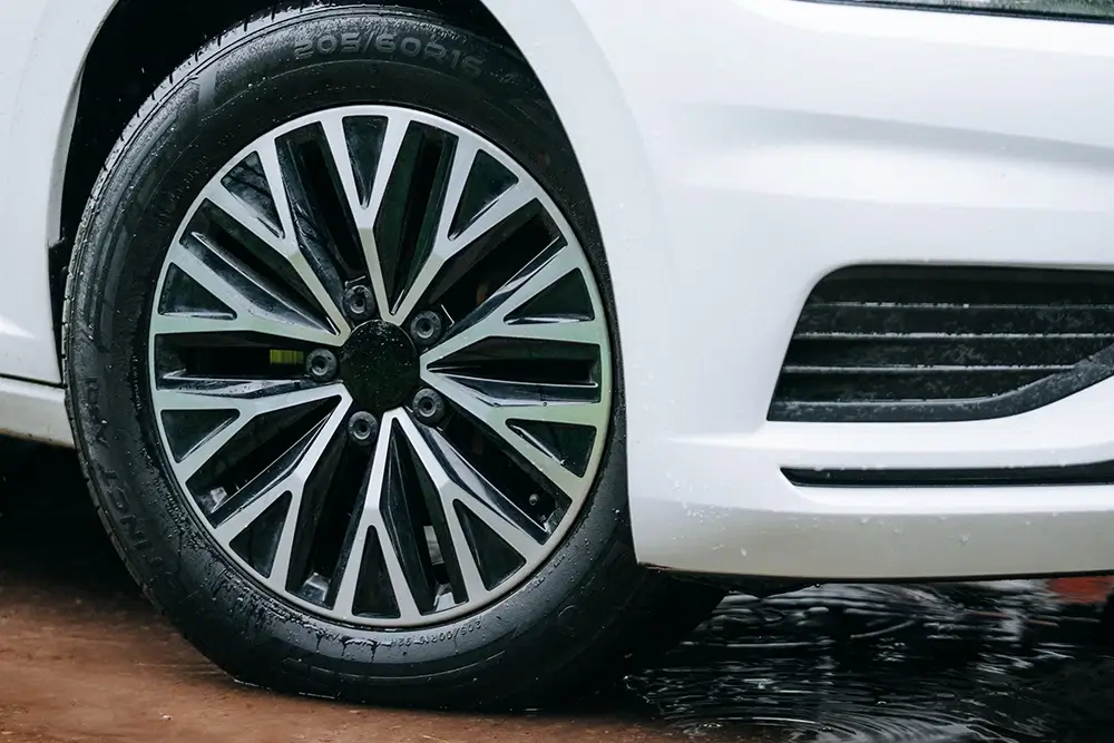 White sedan showing 205/60R16 tires and multi-spoke alloy wheel on wet pavement