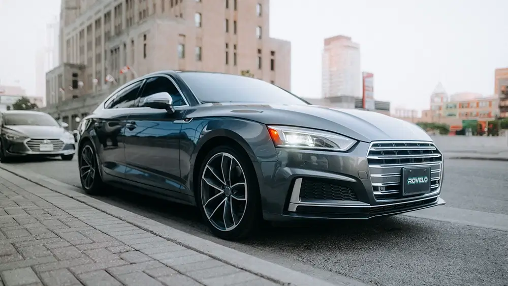 Sleek gray sedan parked on city street, showcasing performance tires and modern styling in urban setting.