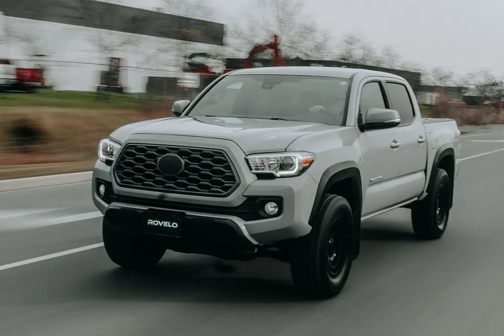 Silver pickup truck with black wheels and performance tires driving on a modern road, showcasing its robust design.